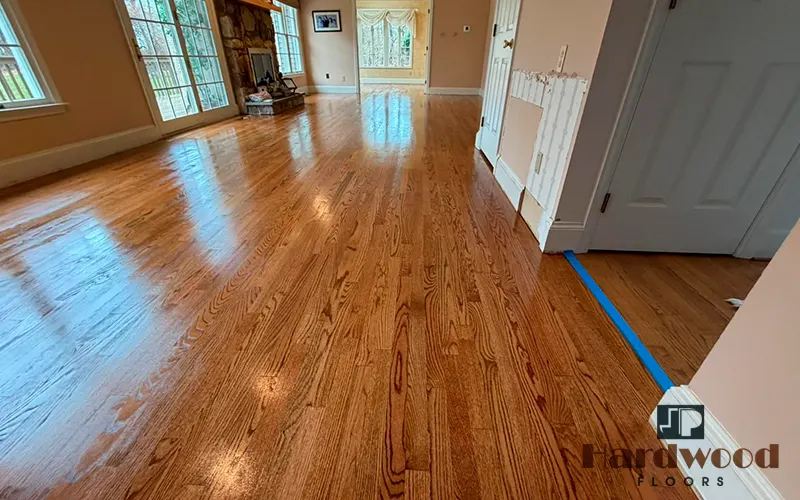 High-gloss amber oak strip hardwood floor reflecting light across a spacious living room by JP Hardwood Flooring.