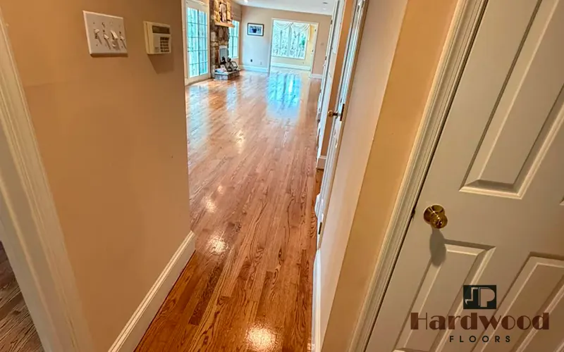 View down a residential hallway showing a gleaming amber oak strip floor transition by JP Hardwood Flooring.