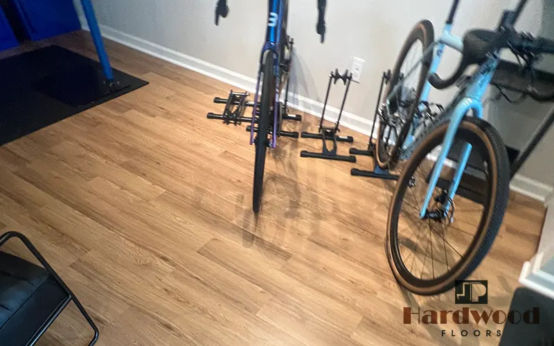 Light oak wood-grain vinyl plank flooring in a home gym or bike storage room by JP Hardwood Flooring.
